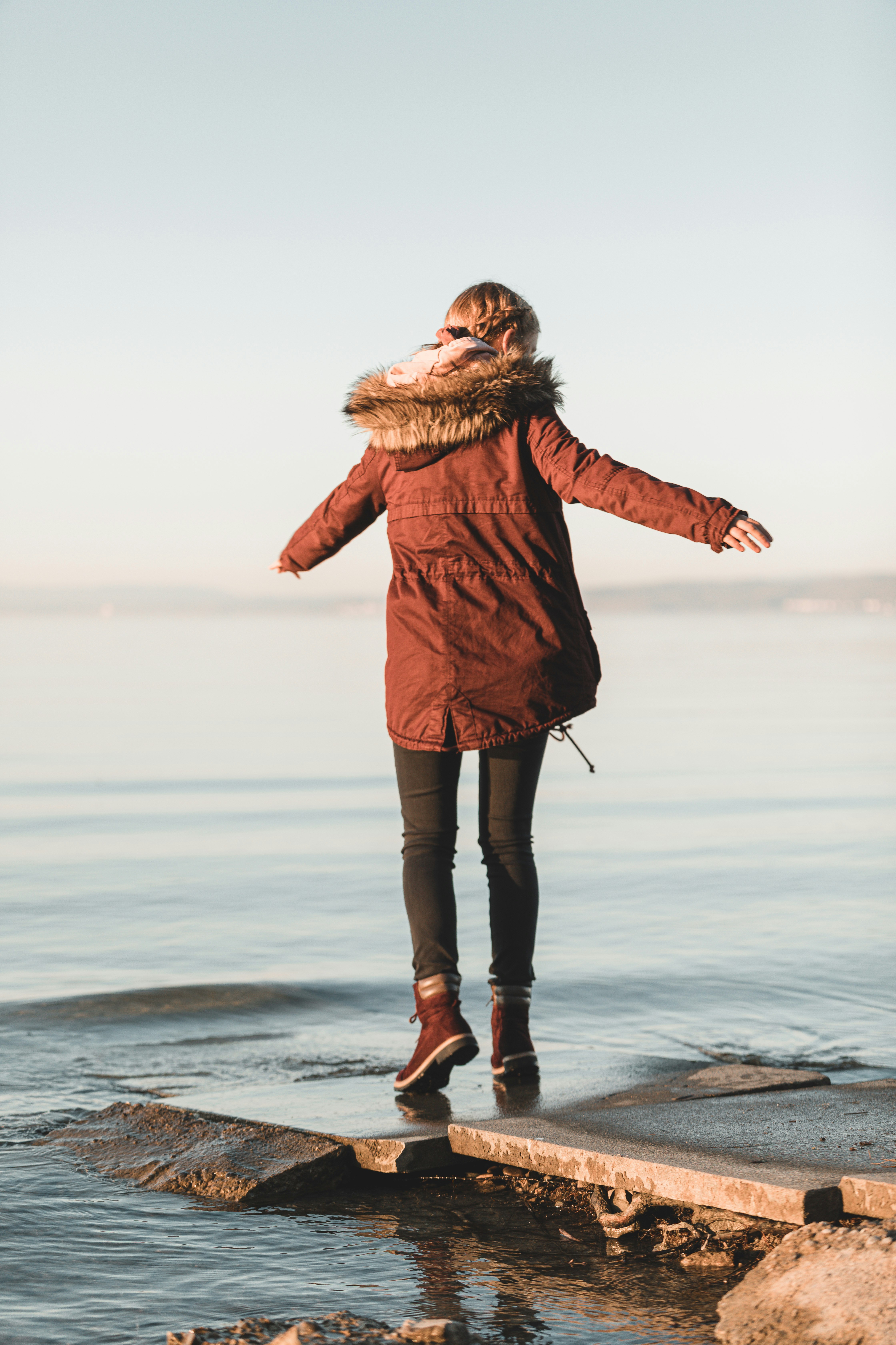 woman in brown coat standing on seashore during daytime